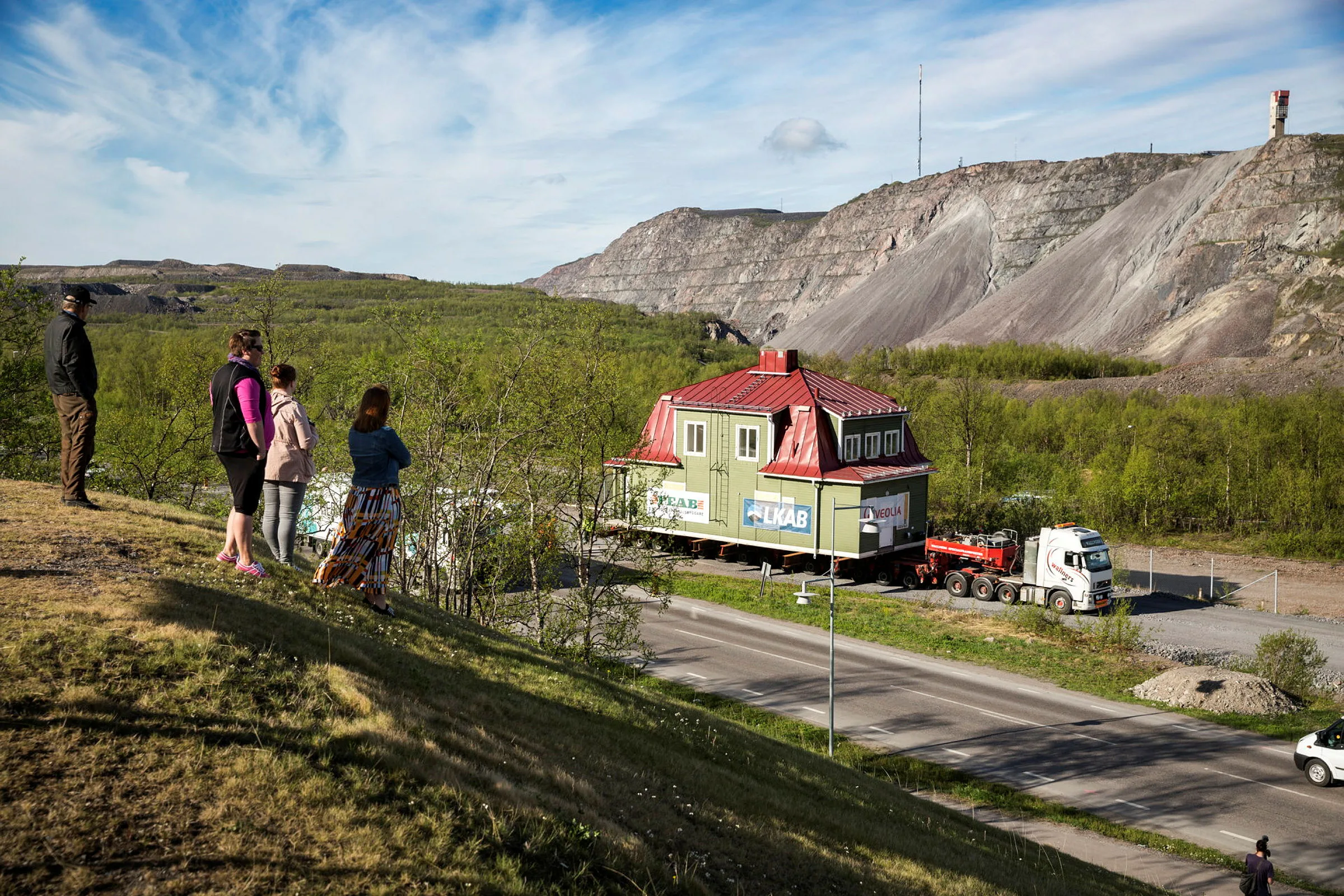 En familj tittar på hur ett hus flyttas i Kiruna. I bakgrunden ser man gruvan.