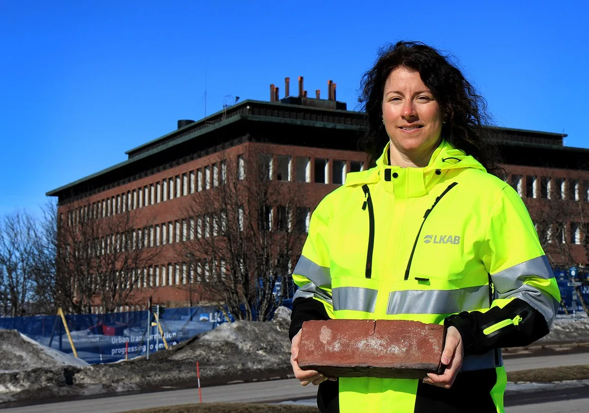 Kvinna i varselkläder håller i tegelsten framför Kiruna stadshus.
